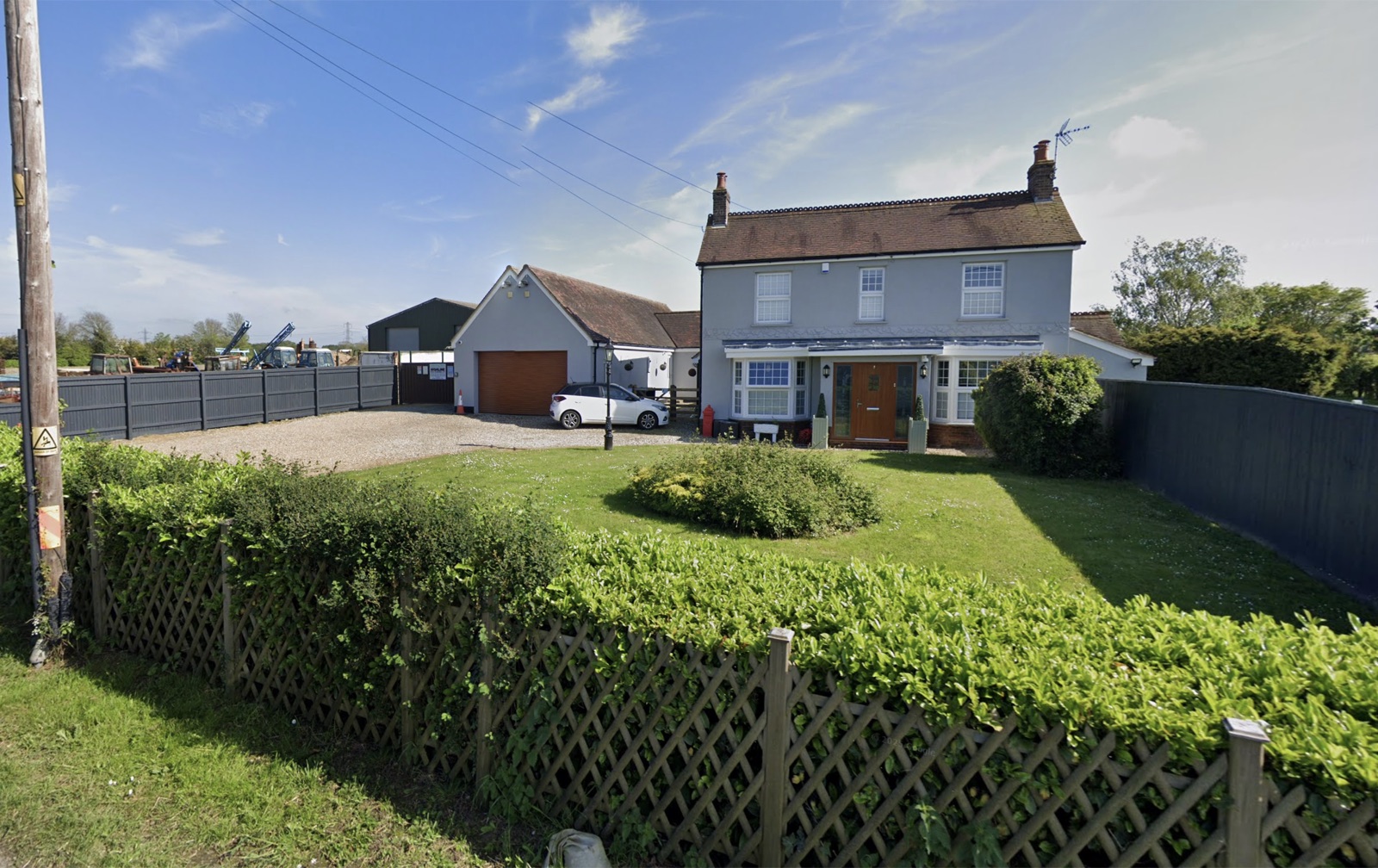 The front of Greenacres, showing the grey house, gravel drive, lawn and hedge